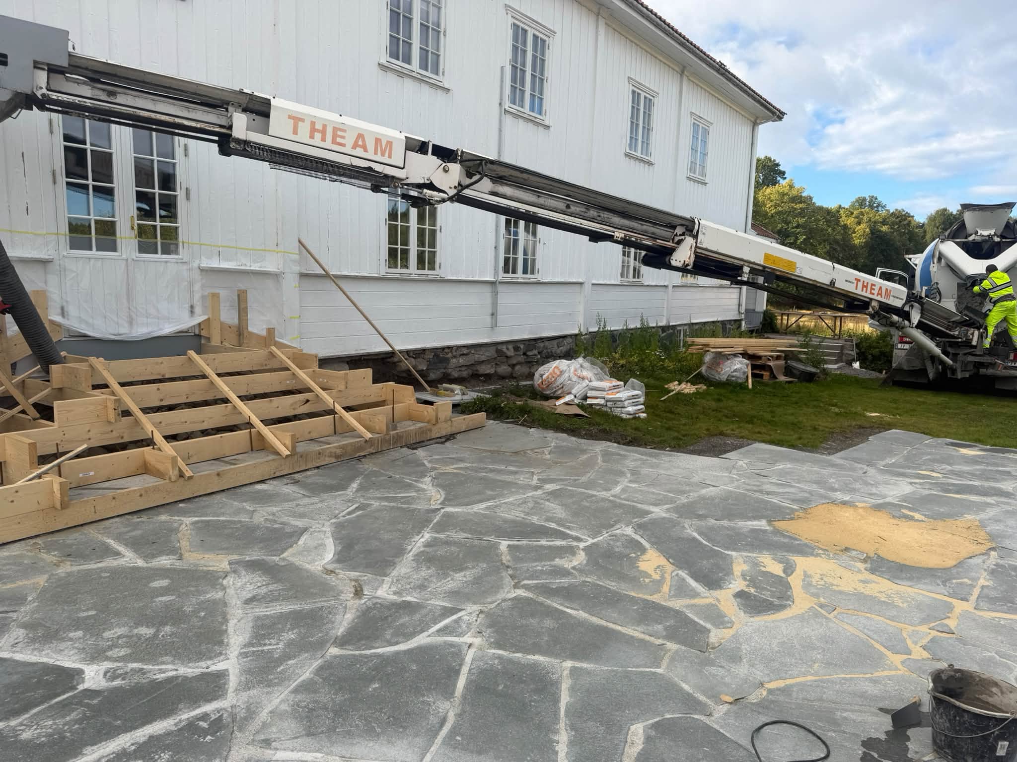 Forskaling ved inngangspartiet til et hvitt trehus, med betongarbeid i gang